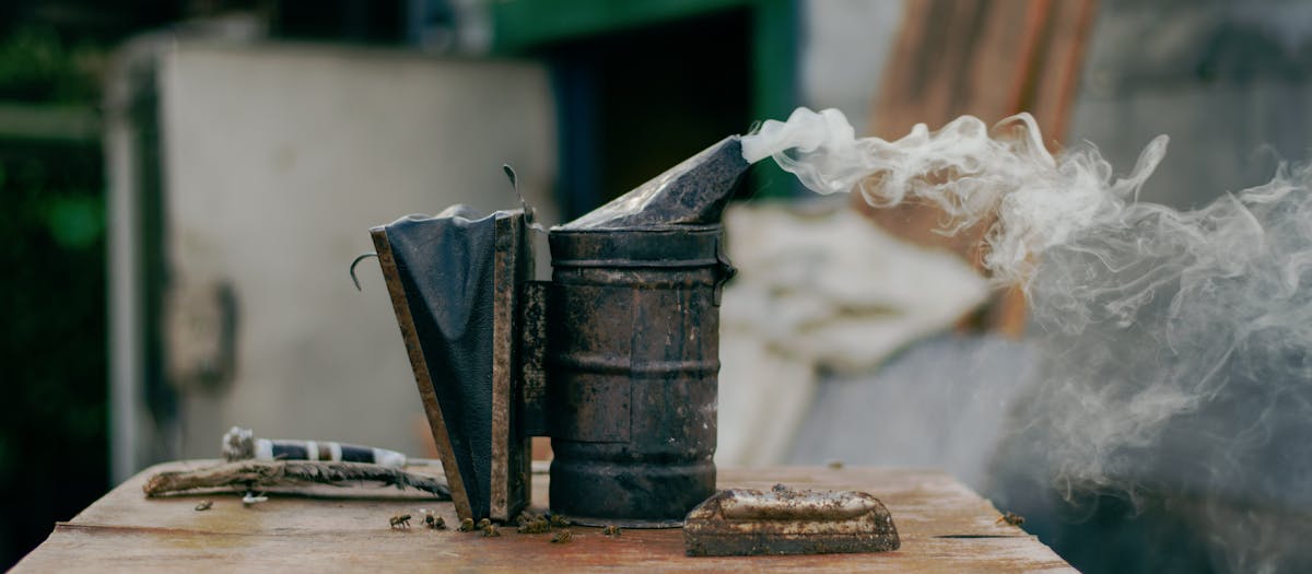 Close-up of a bee smoker releasing smoke on a wooden surface, outdoors.